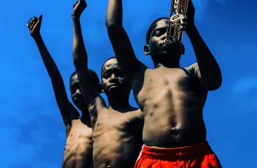 Three happy children raising their arms with a trumpet under a blue sky. Derrick Ofosu Boateng, Music Makes The Pain Fade, 2019